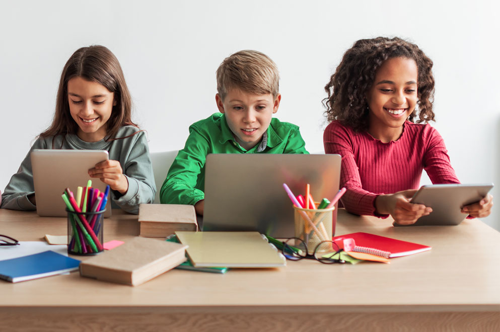 An overhead view of a middle school student writing in a notebook and watching a teacher speak on a laptop