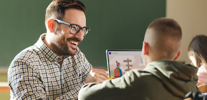 Educator smiling and helping elementary student at their desk while they're using a laptop